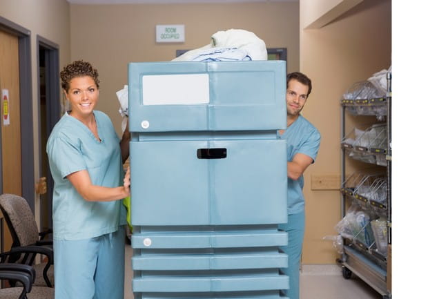 Female and male nurses pushing trolley filled with linen in hospital hallway