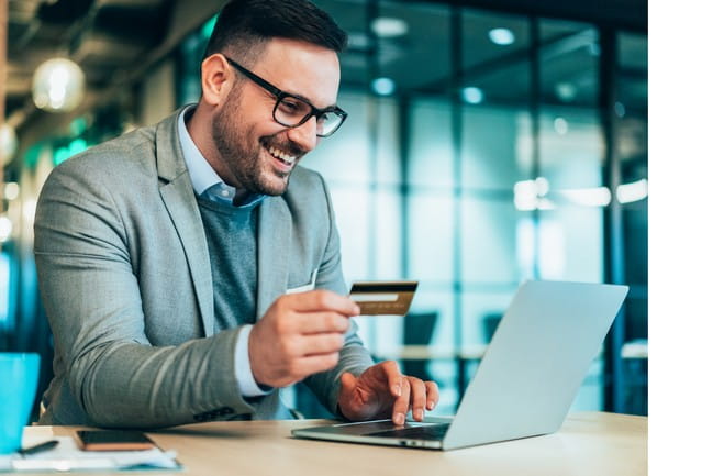 A person using a laptop computer holds a credit card while sitting at a desk.