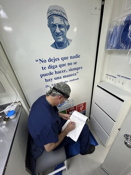 Dr. Edgar Rodas writes in a notebook while in the Cinterandes mobile unit, appearing in front of a photo and quote from his father.