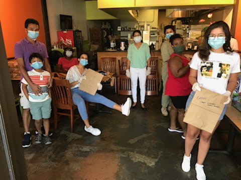 A group of people pose together in a restaurant as they pack food. 