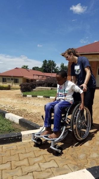 Holly Knapp pushes a child in a wheelchair in Uganda.