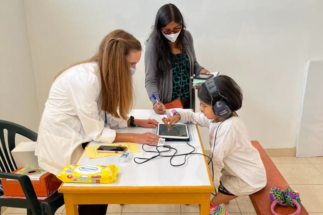 Megan Dempsey assists a child with a hearing test in Peru.