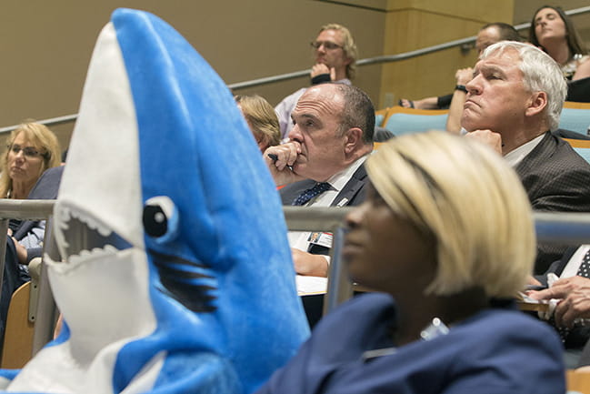 Person dressed as a shark sitting among various people in an auditorium