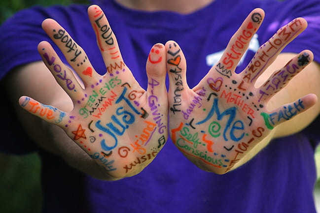 A pair of Caucasian hands with positive words written all over them in magic marker