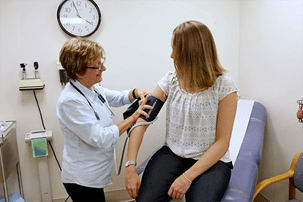 A Caucasian nurse putting a blood pressure cuff on a young Caucasian woman with blonde hair
