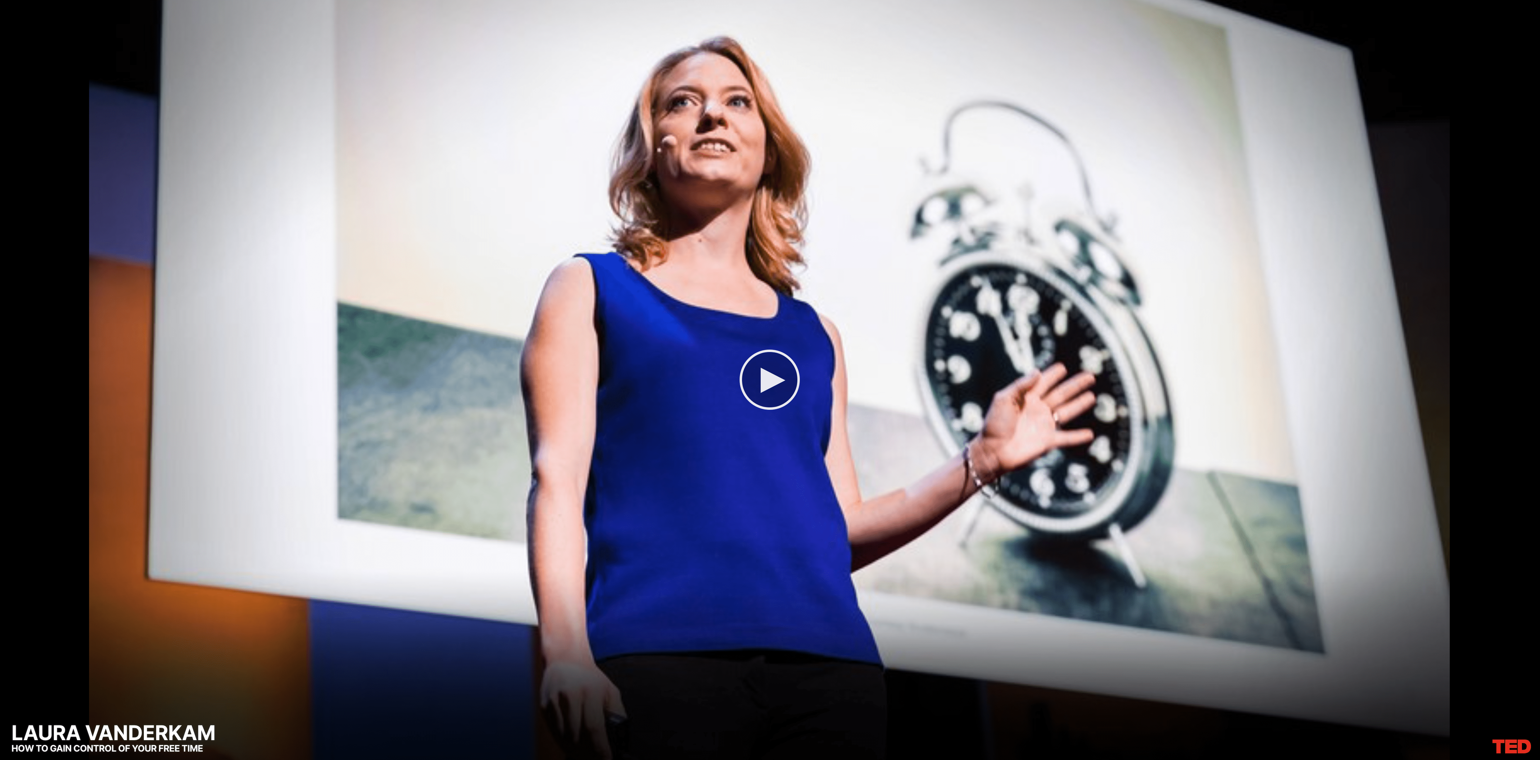 Woman in a blue shirt standing and talking in front of a screen with an alarm clock projected onto it.