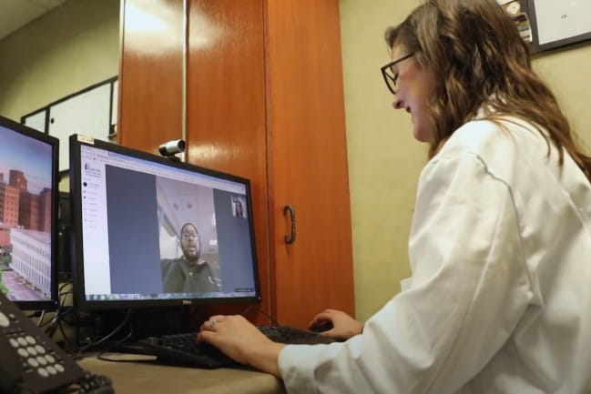 Care team member working with a patient via telehealth using desktop computer and camera.