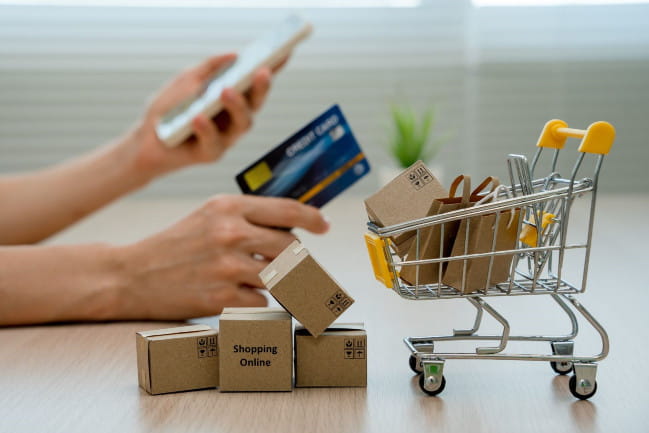 Person holding a credit card next to a mini shopping cart filled with boxes.