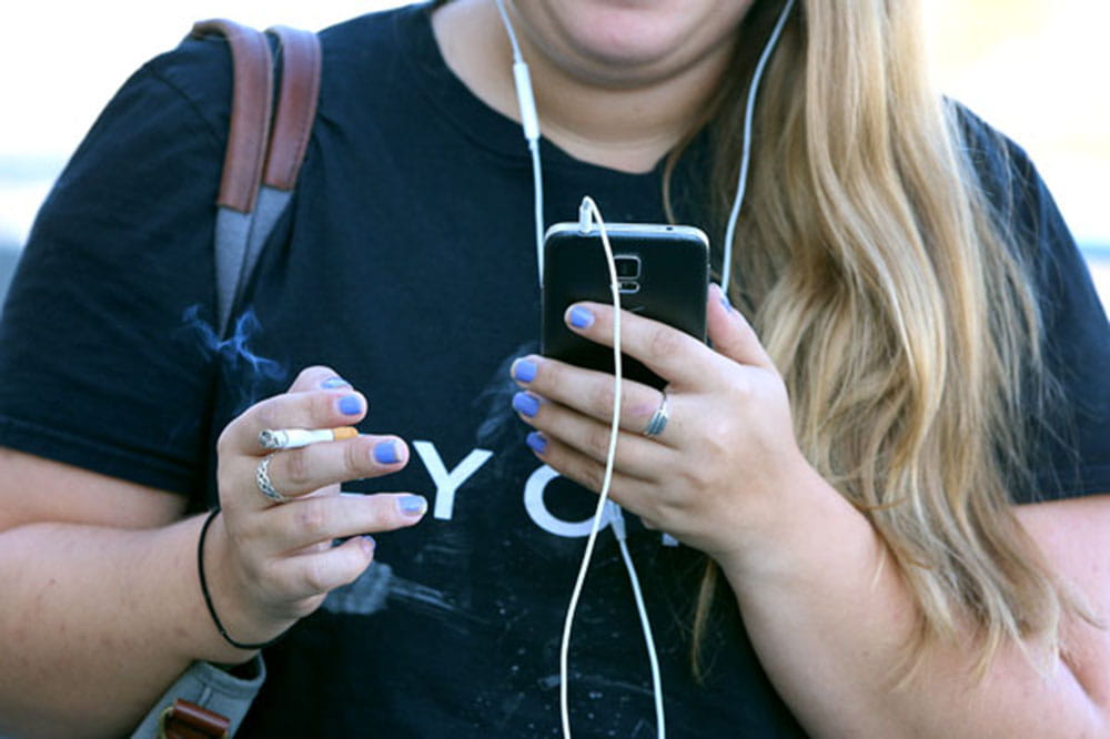 Young woman smoking while using smart phone