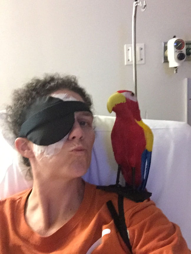 Cara Mathis in hospital bed with stuffed parrot on shoulder
