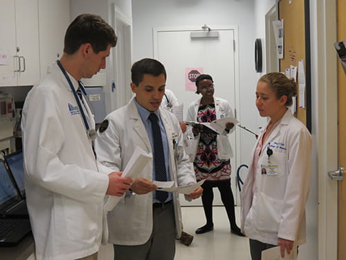 Three medical students look at notes and talk in a hallway