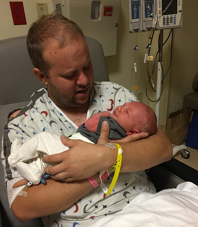 Donnie Yavelak in hospital gown holds his newborn son. 