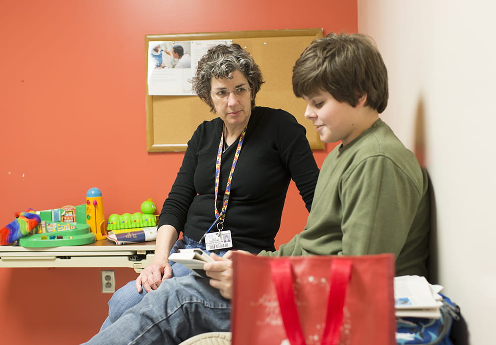 Dr. Jane Charles sits with a young patient in an exam room 