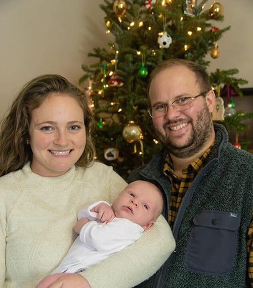 Pamela and Donnie Yavelak with baby Levi in front of a Christmas tree. 