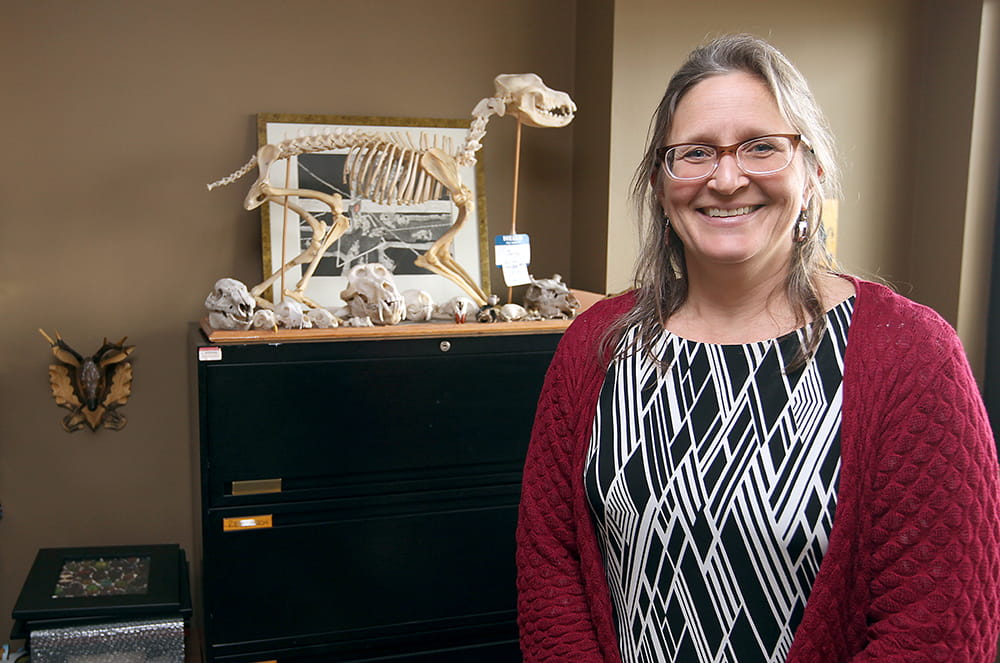 Kristi Helke stands in her office in front of a small animal skeleton
