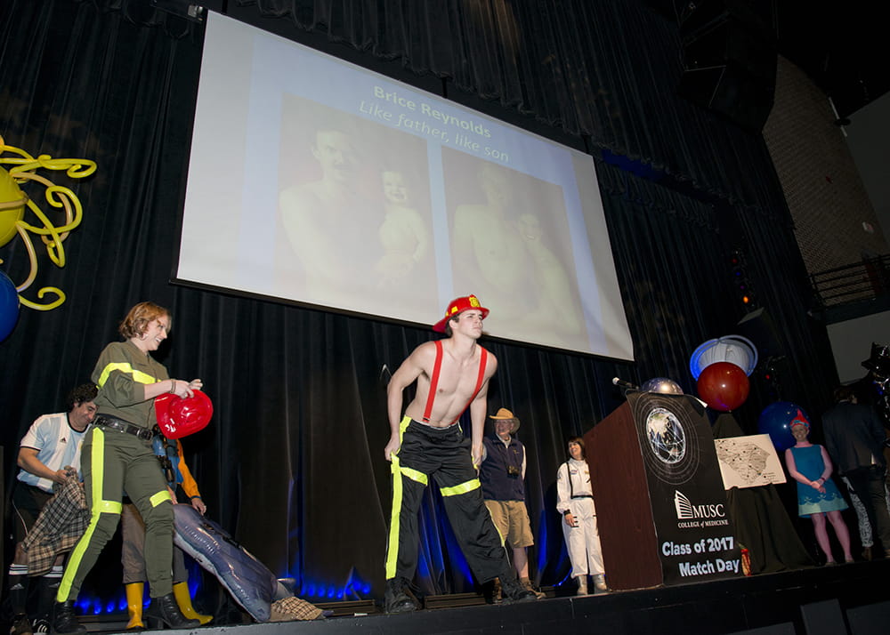 A student dressed as a firefighter is poised to strip off his pants on stage