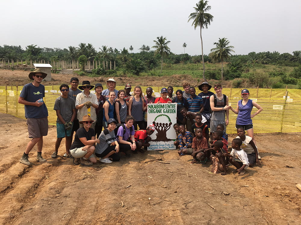A group of visiting Americans and local Ghanaians pose in front of a sign for what will be a garden 