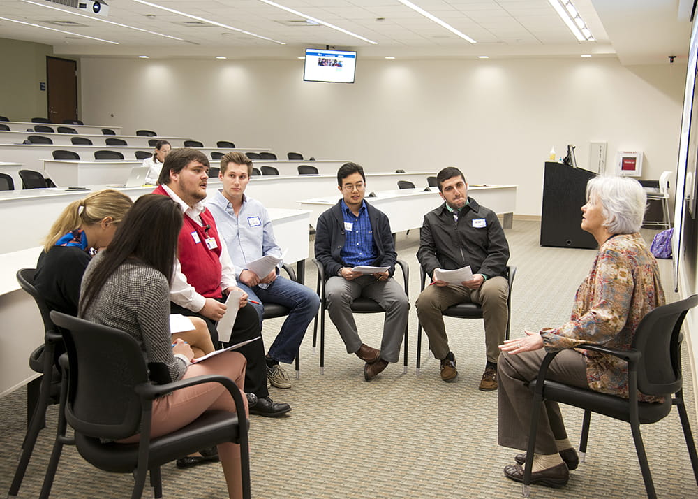 Students sit in a circle facing an employee portraying a family member. 