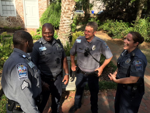 four officers -- three male and one female -- stand in a semi-circle and laugh outside 