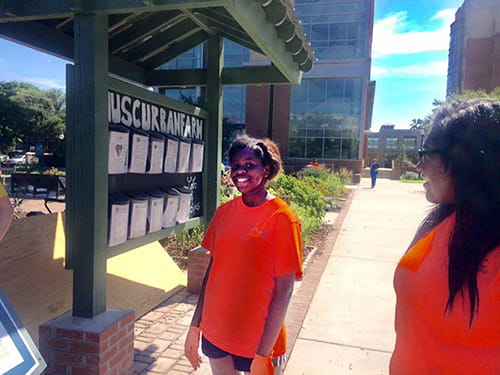 Young people in orange shirts stand in front of a kiosk at the garden at MUSC. 