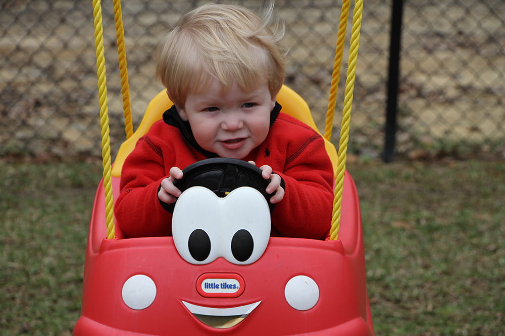 A little boy sits in a plastic swing shaped like a smiling animated car