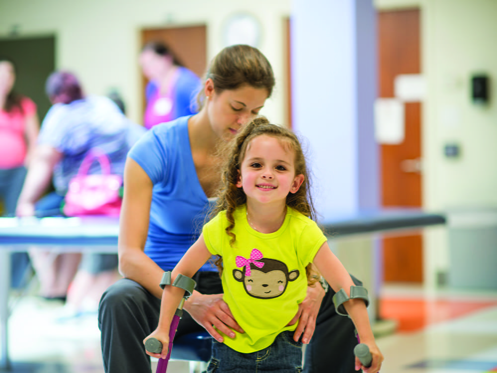 A physical therapist works with a little girl using crutches