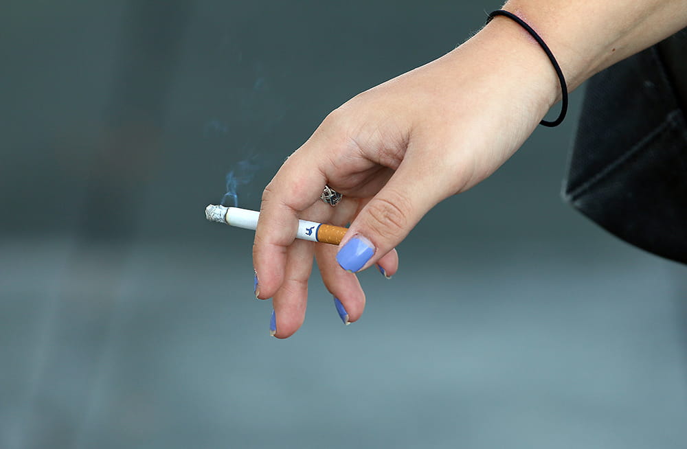 a young woman's hand with chipped blue nail polish holds a lit cigarette
