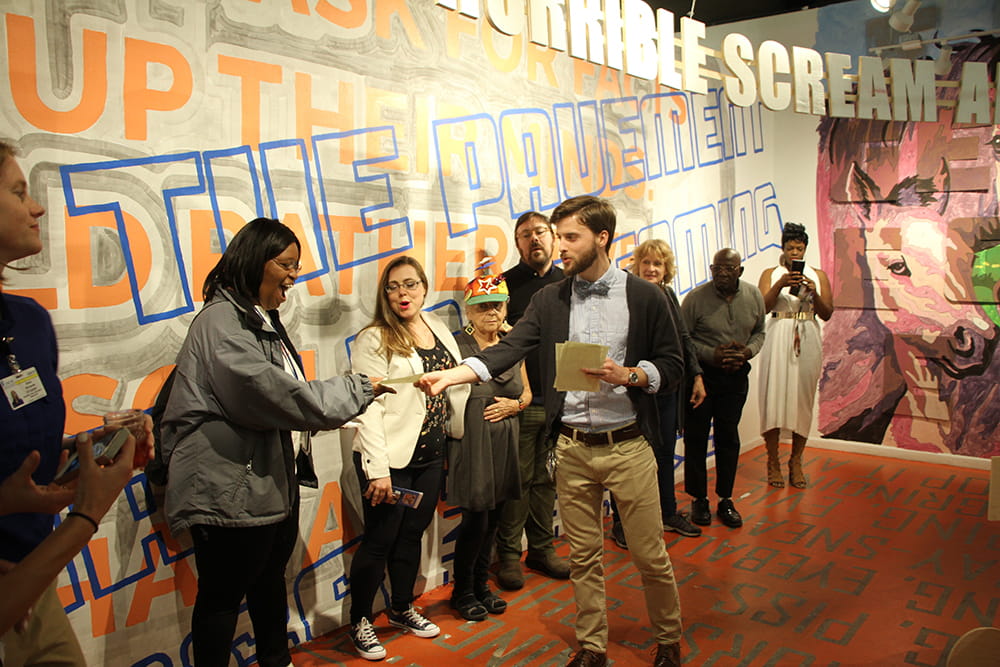 a young man hands a woman a gift card as people look on 