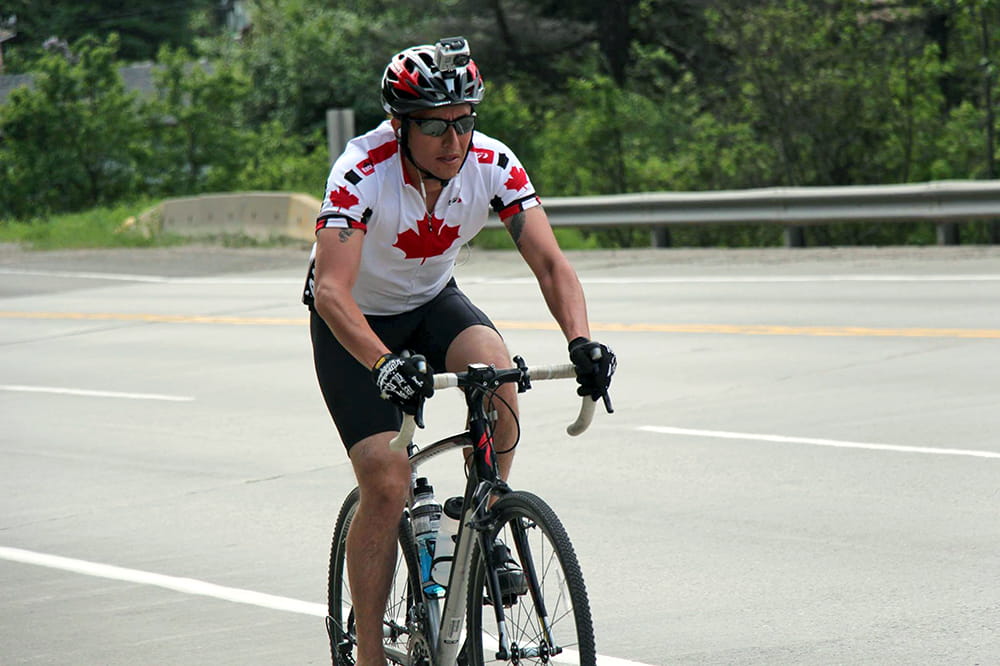 A man rides a bicycle down a highway wearing a Canadian jersey