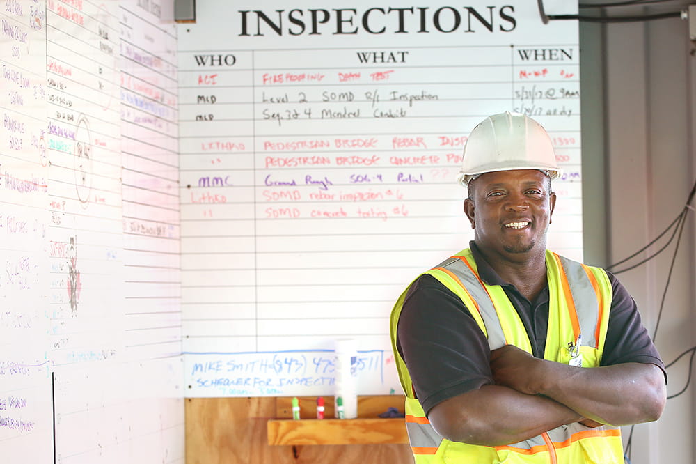 Mike Smith poses in hard hat and safety vest in front of an "inspections" white board