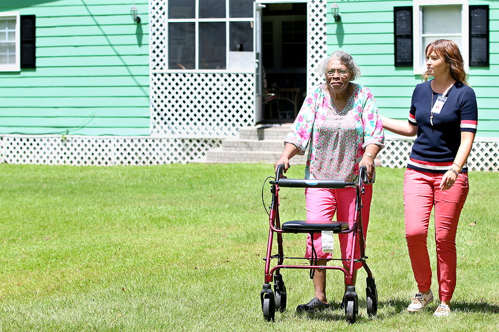 a young woman walks with an older woman using a walker on grass 