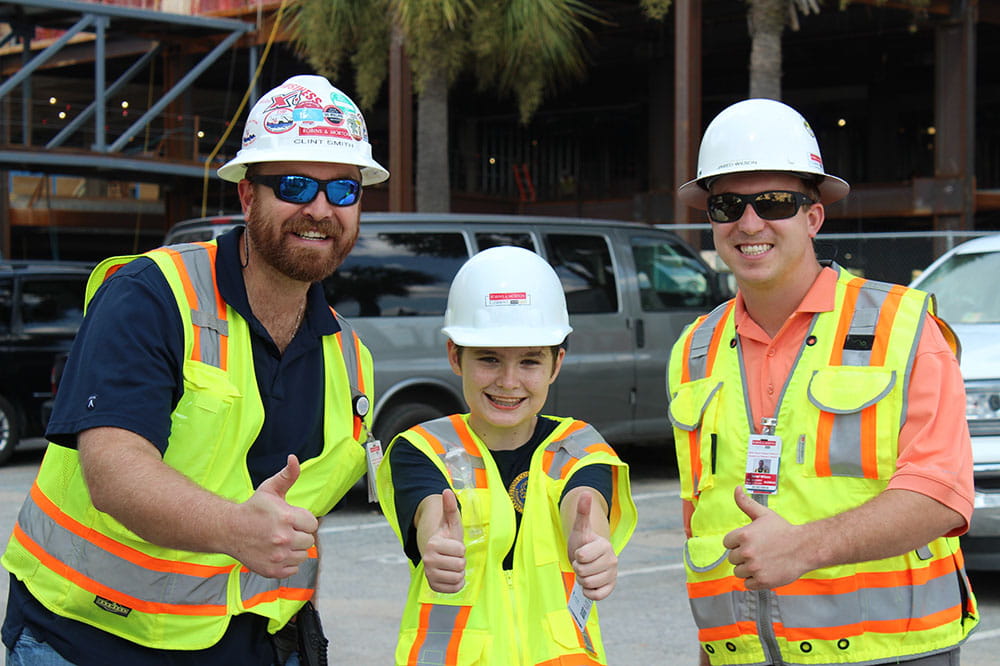 Robins & Morton project engineer Clint Smith, left, 14-year-old Vincent Hild-Mullins and Robins & Morton assistant superintendent Jared Wilson give a thumbs-up during Vincent's tour.