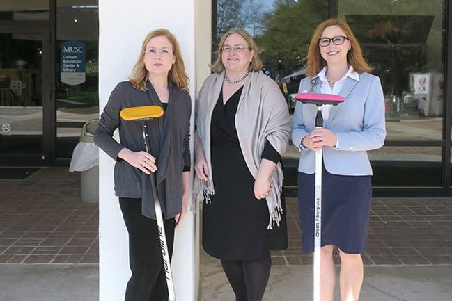 Curling Club founder Amanda Smith, from left, joins fellow members Jody Latham, Controller's Office-Bursar, and Jilian Filan, MUHA Decision Support Services, as they show off their curling brooms.