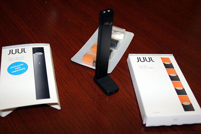 On the left, the package for a reusable Juul device that cost $38.99 at a Charleston vape shop. In the center, the Juul device itself, which looks like a flash drive, with nicotine-containing pods behind it. On the right, the package the $16.99 mango-flavored pods came in.