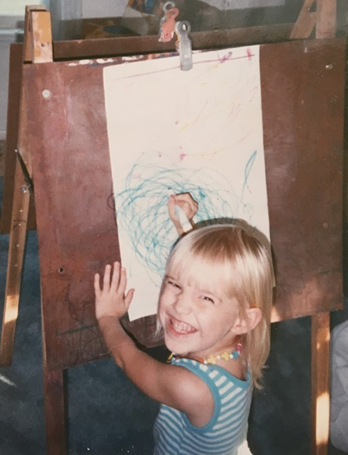 a young girl smiles as she look up from her art easel 