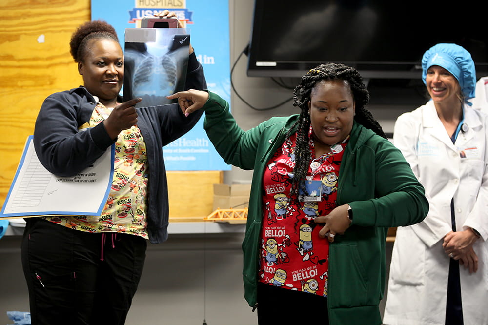 two women hold up a x-ray of a child's chest to show a group of visiting kindergartners