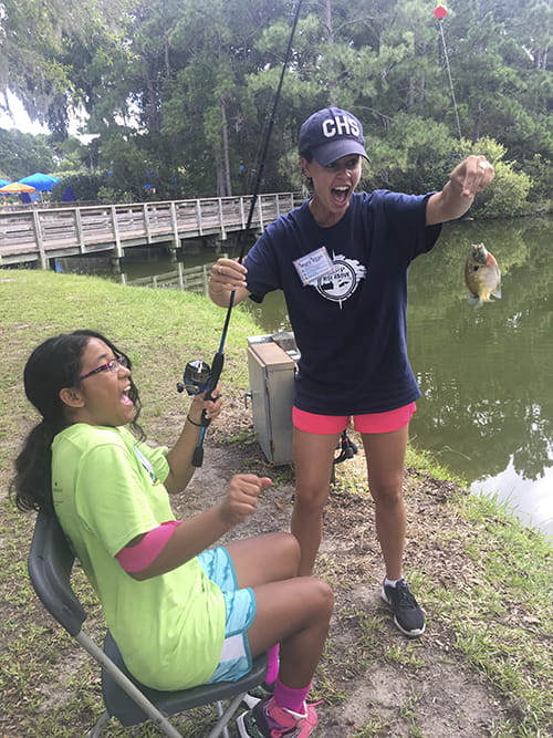 A girl and a camp counselor shriek in delight as they look at a fish the girl just caught