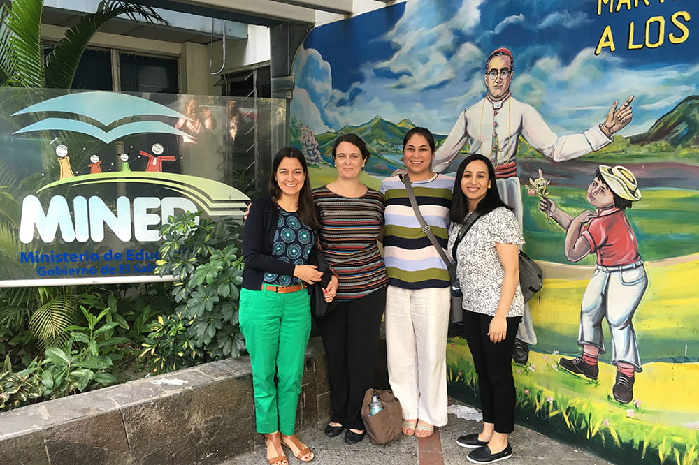 Four women pose in front of a colorful mural at the Ministry of Education in El Salvador