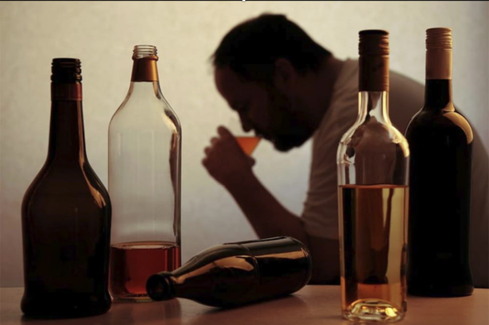 A man in silhouette drinks, framed by alcohol bottles