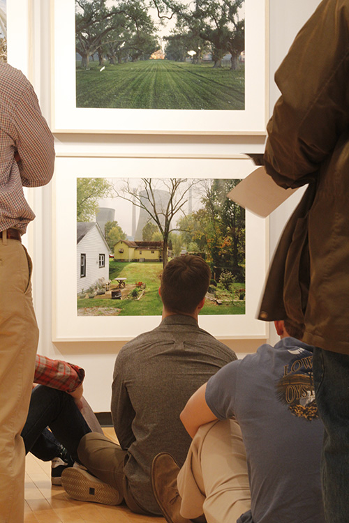 people sit on an art gallery floor looking at photographs