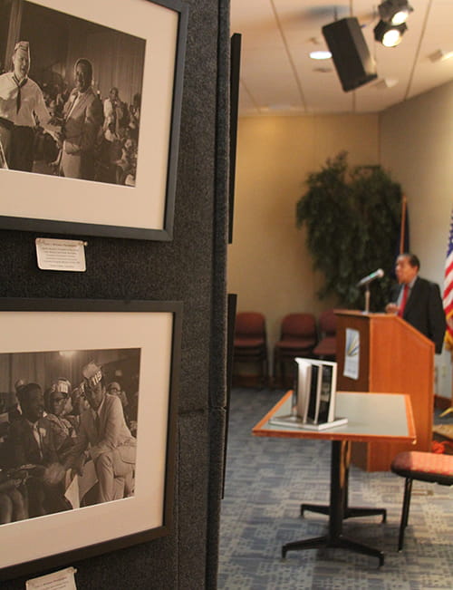 A display of old black and white photos, while in the background the photographer speaks at a podium 
