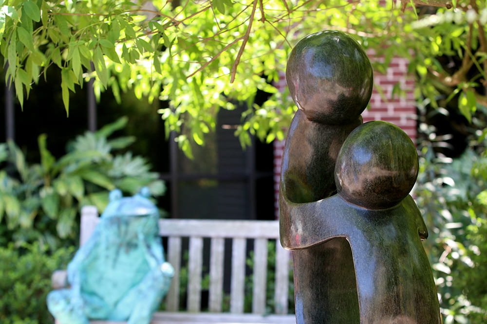 a closeup of the abstract statue of two figures in the foreground and a human-sized frog statue in the background