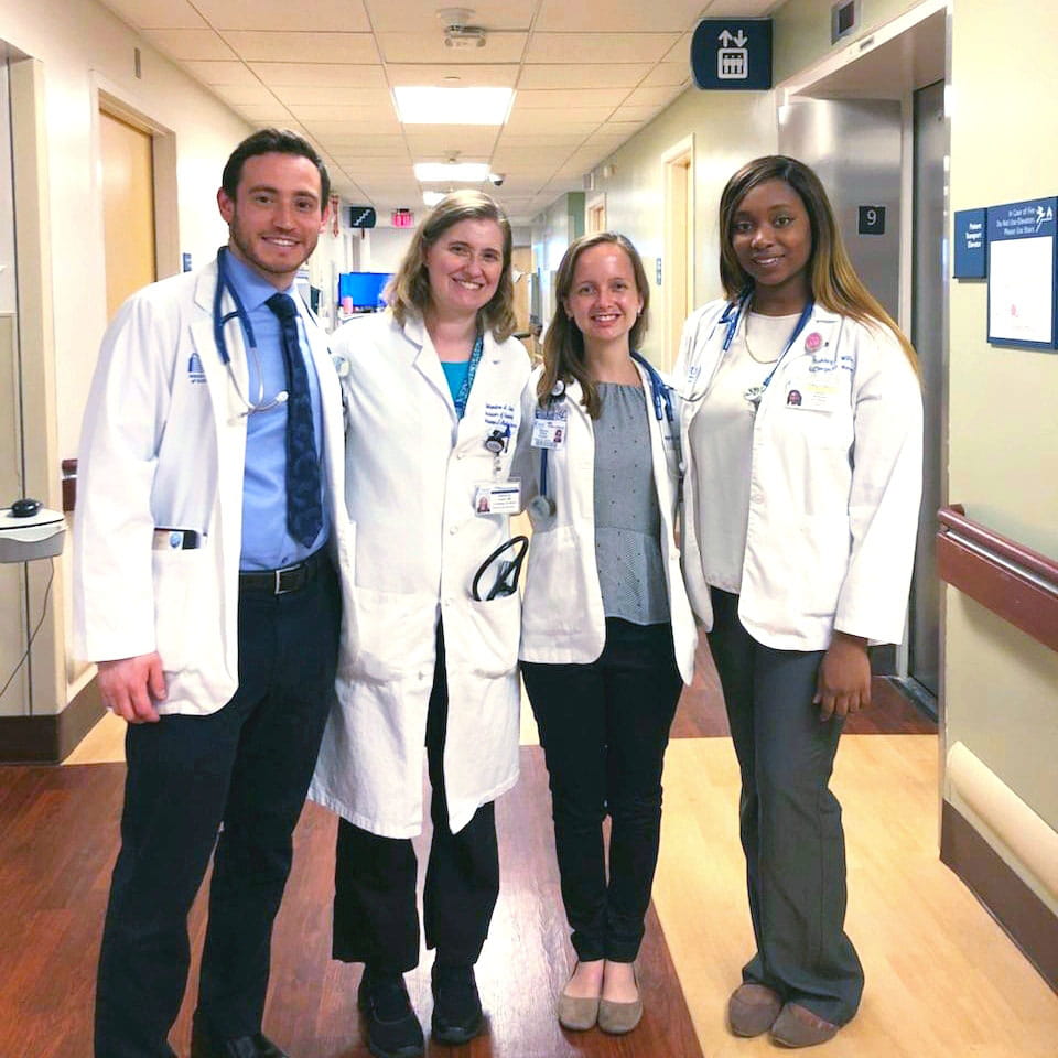 group photo of doctor in a white coat with three medical students in a hospital hallway