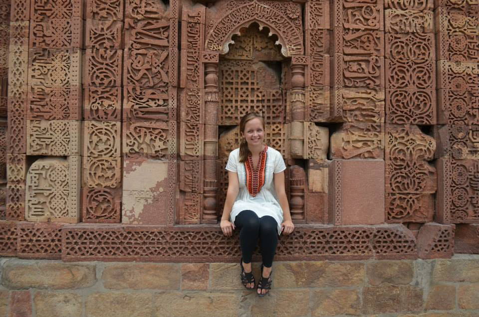Shannon McGue sits by an elaborately carved tower in Delhi