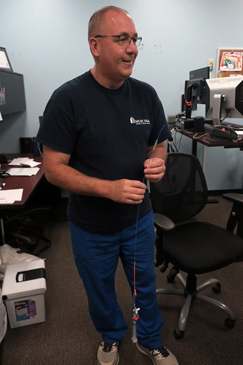 A man stands in an office and holds a long catheter tube called a REBOA