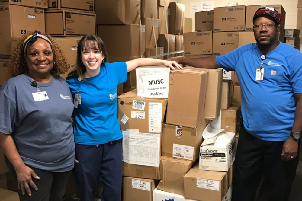 Three people pose by boxes of supplies 