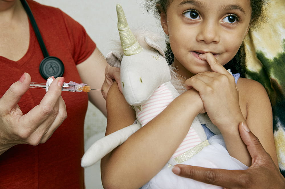 a girl clutches a stuffed unicorn as she's about to get a flu shot