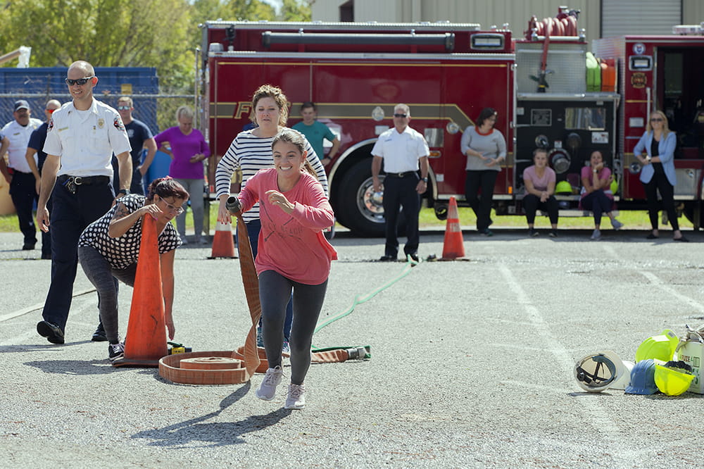a grinning woman races toward the camera holding a fire hose