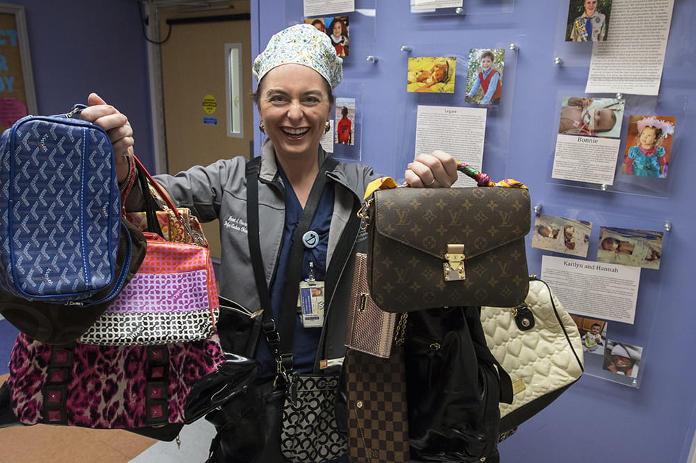 A woman in scrubs holds up dozens of purses on her arms