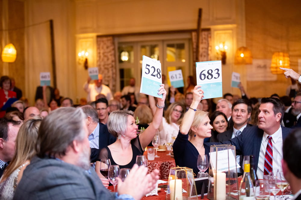 people at dinner table raise cards at an auction 